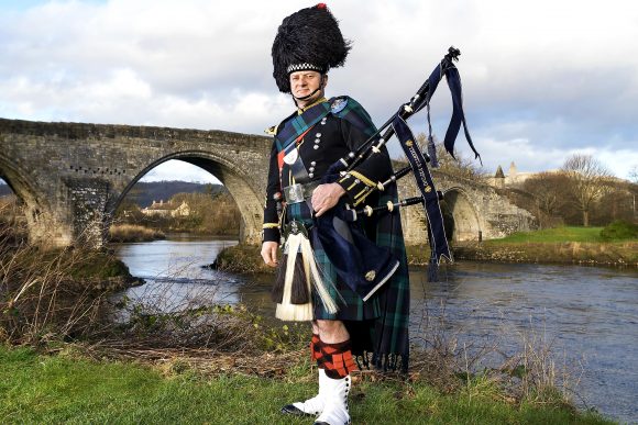 Wedding Piper Scotland in full regimental uniform with Stirling Bridge and Wallace Monument behind